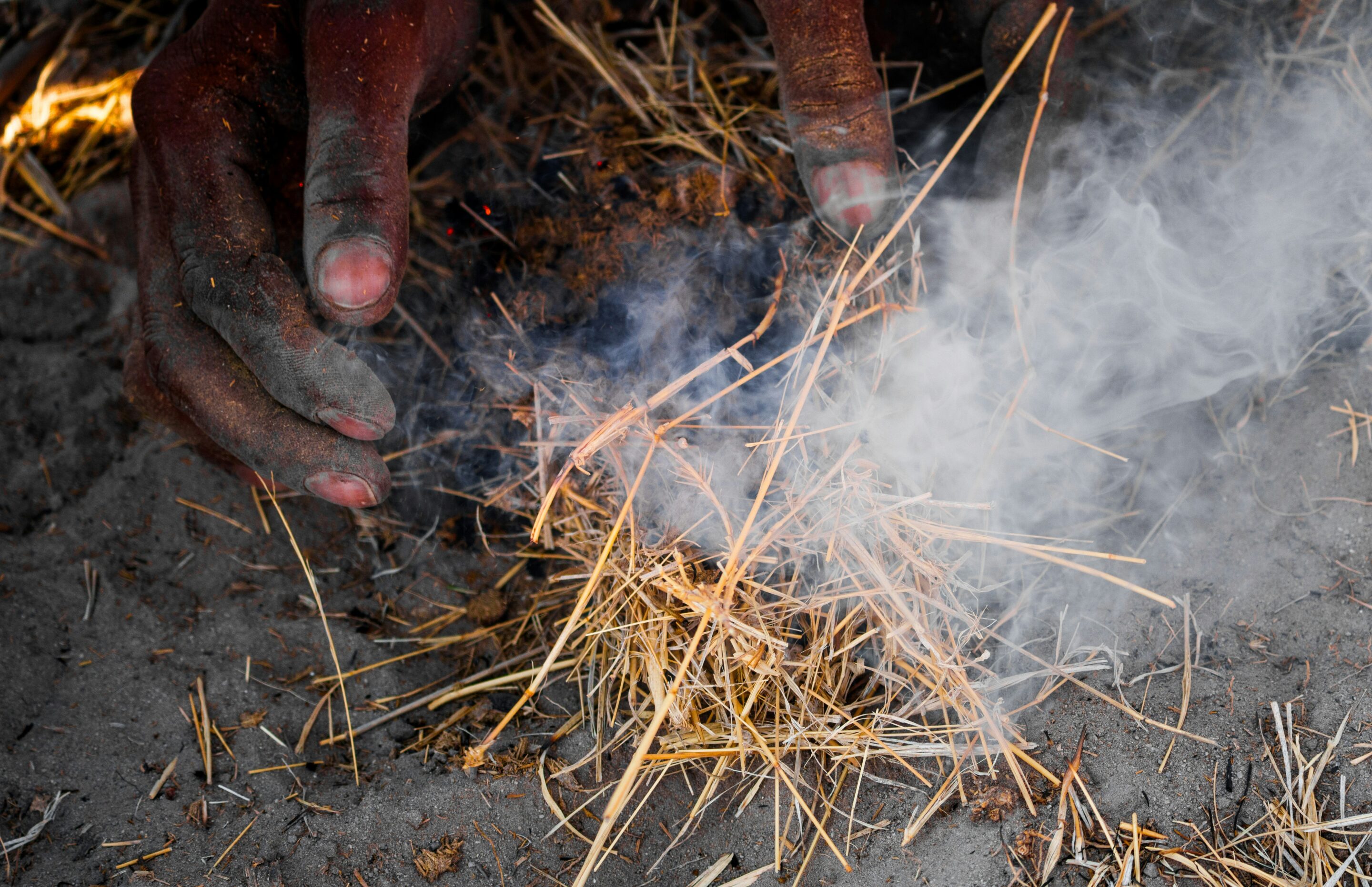 Manos encendiendo fuego con paja, con humo, método tradicional