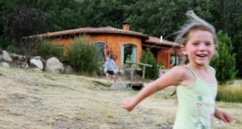Niña corriendo feliz frente a una casa de bioconstrucción en la finca de permacultura Salama